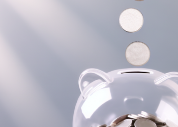 An image of silver coins falling into a clear piggy bank