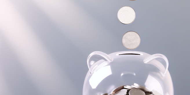 An image of silver coins falling into a clear piggy bank
